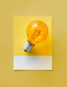 Lit light bulb on yellow background.