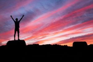 Man standing triumphantly on top of a mountain.